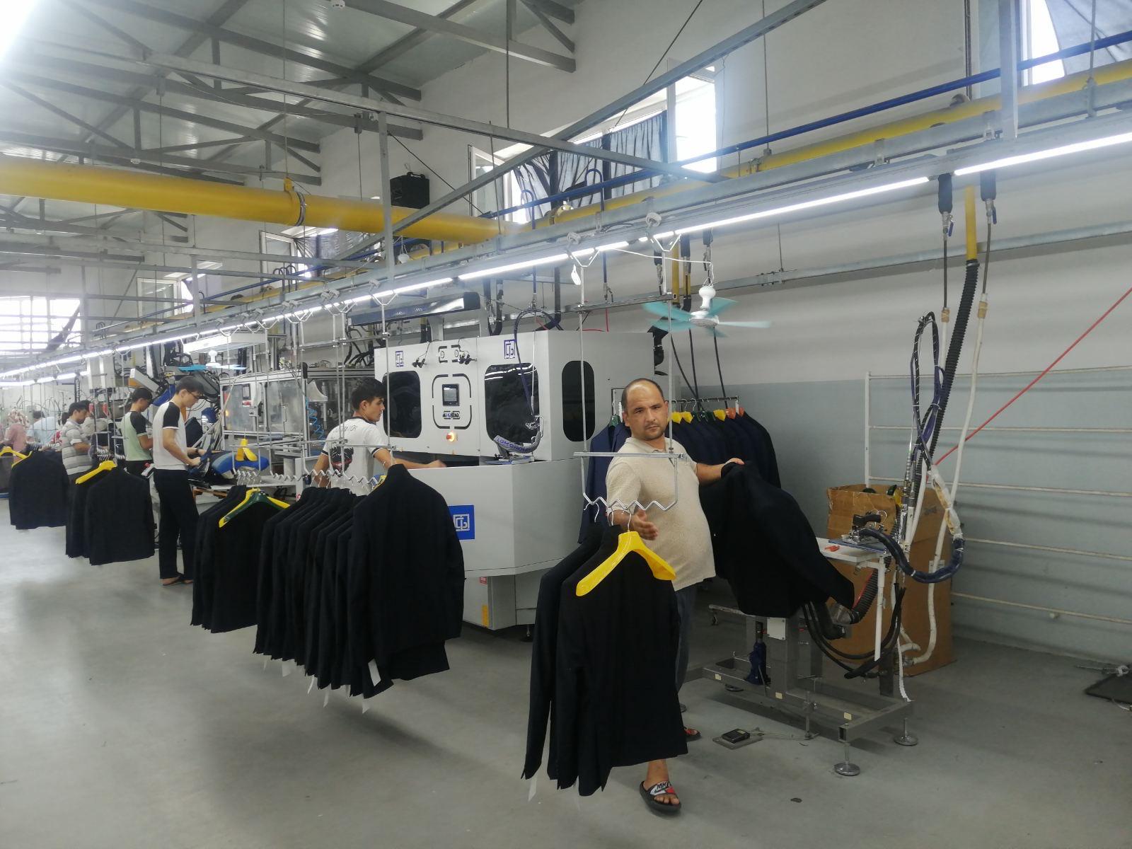 Workers handling dark jackets beside garment processing equipment